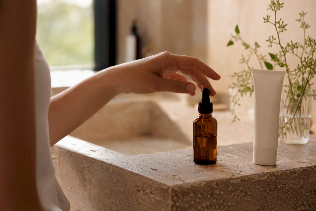 Hand holding serum dropper near sunscreen tube