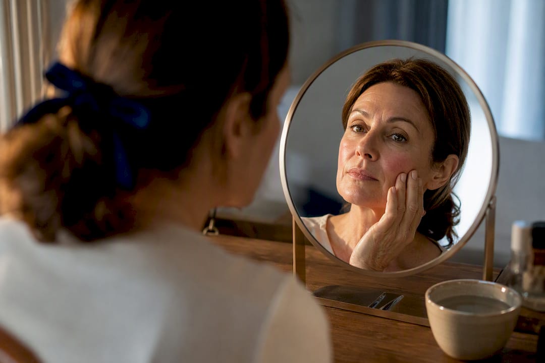 Person inspecting mild cheek redness in mirror