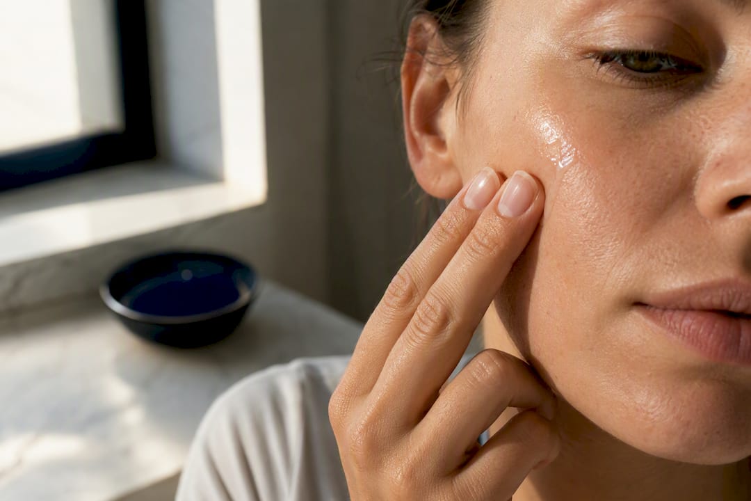 Fingertips applying peptide serum to cheek